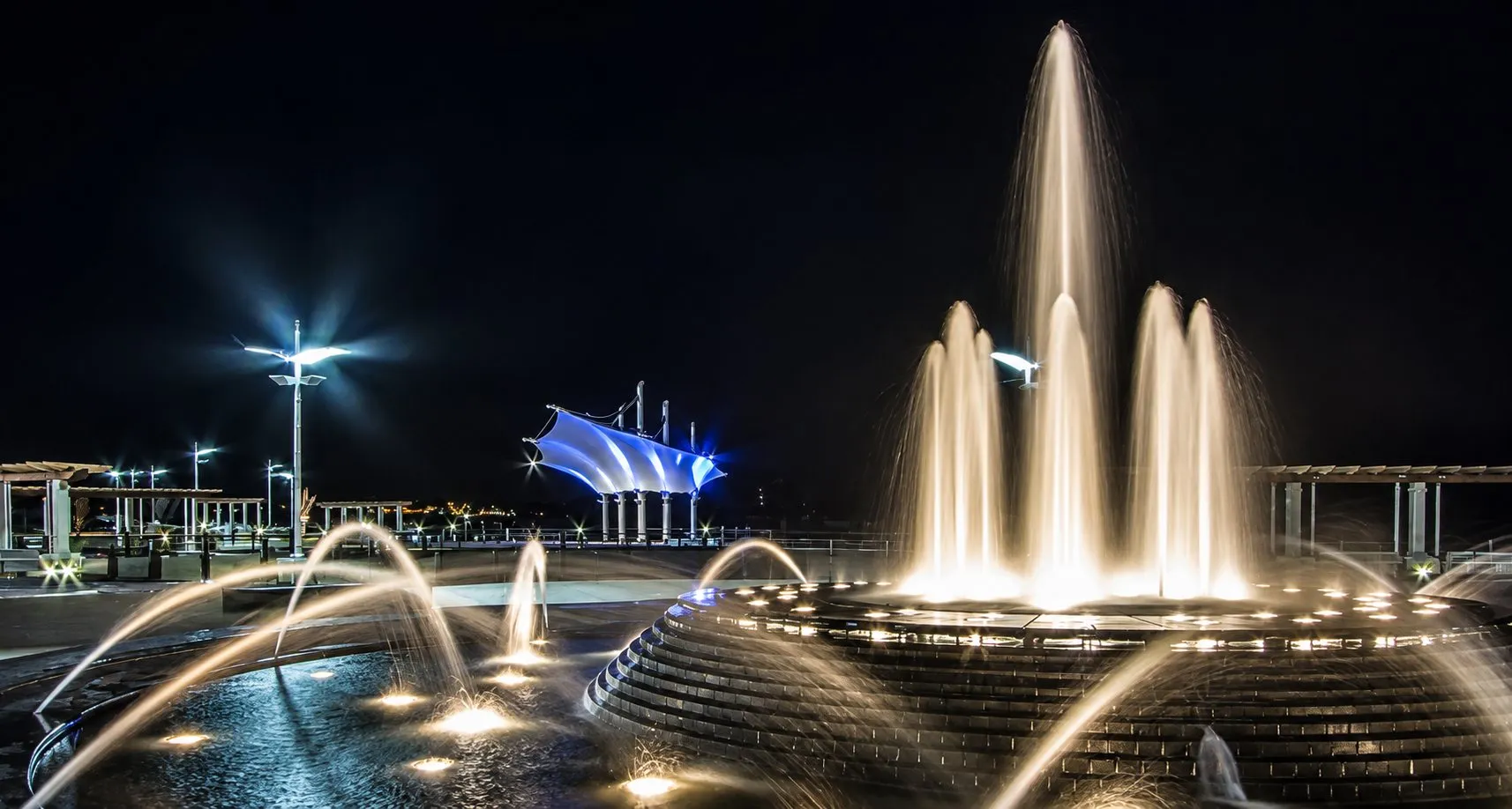 Illuminated fountain jets and arching sprays in a public plaza at night